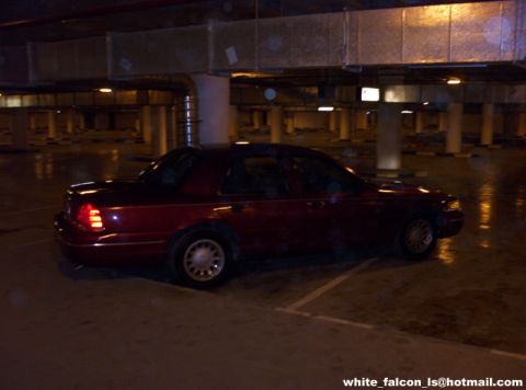 2000 Ford Crown Victoria - A red sedan is parked in a concrete parking garage at night, with wet floors reflecting the lights.
