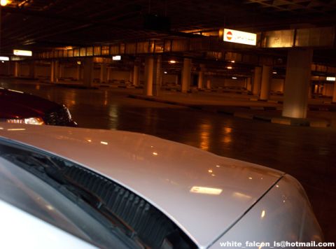 2000 Ford Crown Victoria - A white car is parked in a dark, multi-level parking garage with overhead lights.