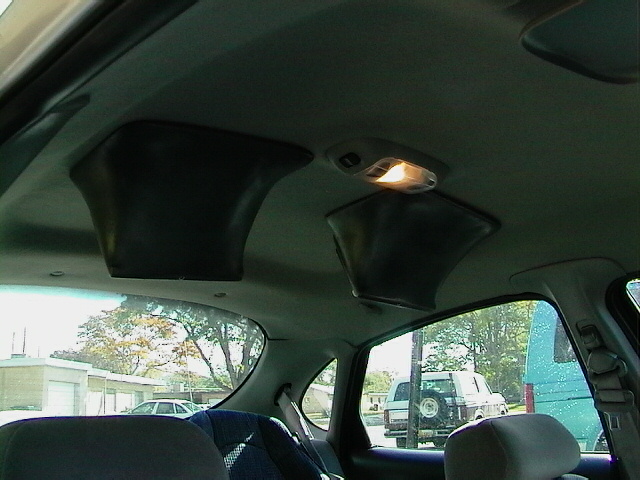 Car interior showing aftermarket speaker pods on the ceiling and a view out the window of other vehicles