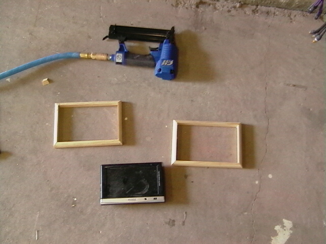 Staple gun with blue hose, two wooden frames, and a small black screen on a concrete floor