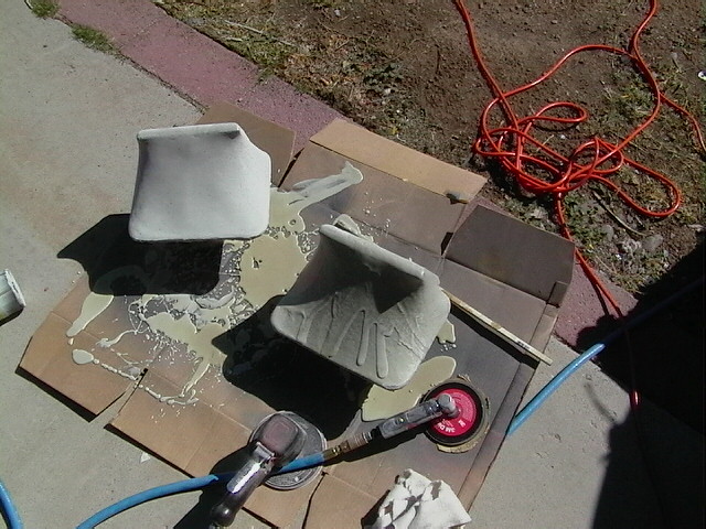 two car body parts on cardboard with sanding tools and orange extension cord