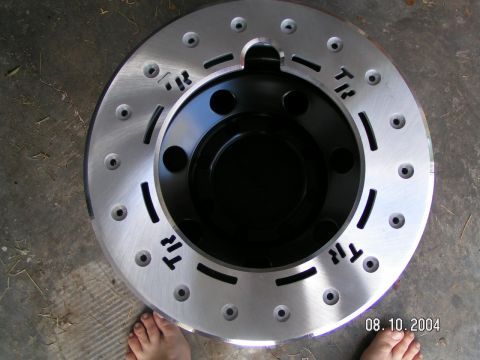 1978 Ford Bronco - A close-up view of a drilled and slotted brake rotor with 'TR' markings, resting on a concrete surface.