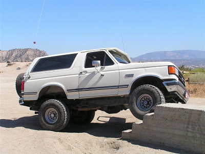 1988 Ford Bronco - A white Ford Bronco navigates an off-road obstacle course on a sunny day.