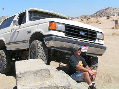 1988 Ford Bronco - Man sits in front of a lifted 1988 Ford Bronco in a desert landscape.