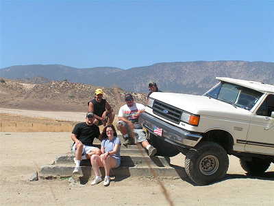 1988 Ford Bronco - A group of people sit on concrete steps next to a white Ford F-Series truck in a dry, mountainous landscape.