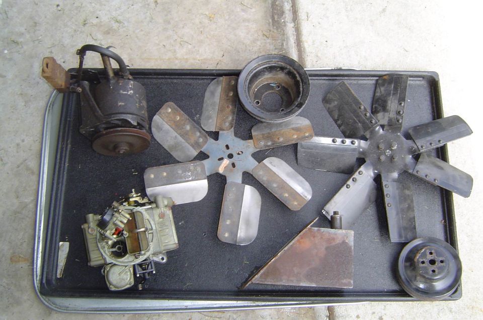 Power steering pump, carburetor, two engine fans and pulleys laid out on a shop mat