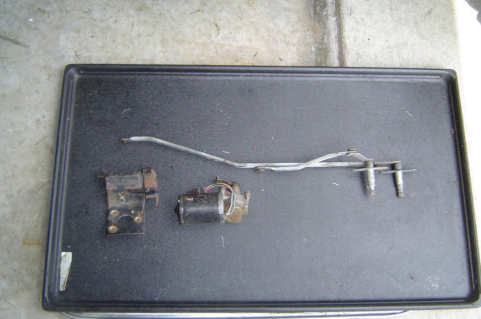 Used wiper motor, mounting bracket and linkage with pivots laid on a black tray