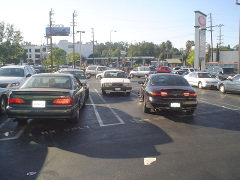 1993 Ford Taurus - A dark sedan is parked in a lot with other vehicles.