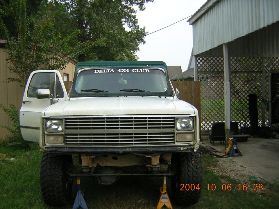 White pickup truck with green top, lifted suspension, and "DELTA 4X4 CLUB" sticker on windshield