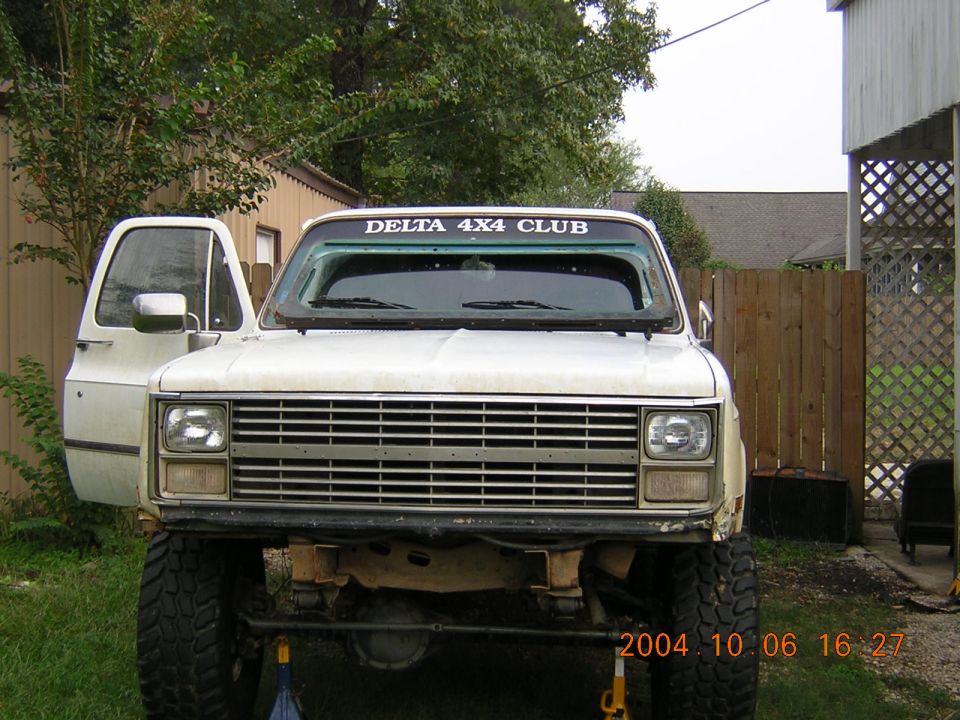Front view of a white lifted pickup truck with the driver's door open. It has a 'DELTA 4X4 CLUB' sticker on the windshield