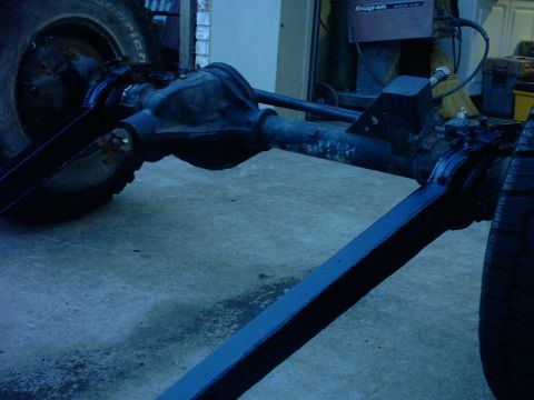 1995 Ford Bronco - Bare front axle assembly sitting on a garage floor out of the vehicle, showing the cast pumpkin housing, axle tubes, knuckles and long fabr…