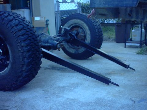 1995 Ford Bronco - A bare solid axle assembly on oversized mud-terrain tires and steel wheels stands on a concrete driveway with two long black-painted leaf s…