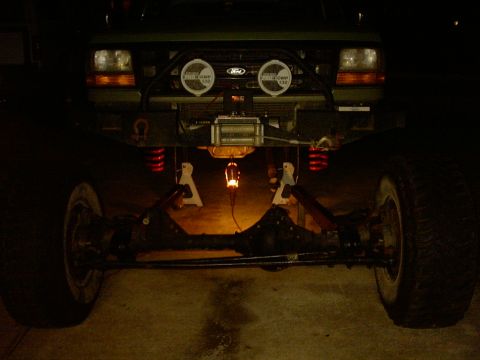 1995 Ford Bronco - Nighttime front view of a Ford truck up on jack stands during front-end work, with a complete solid front axle and steering linkage sitting…