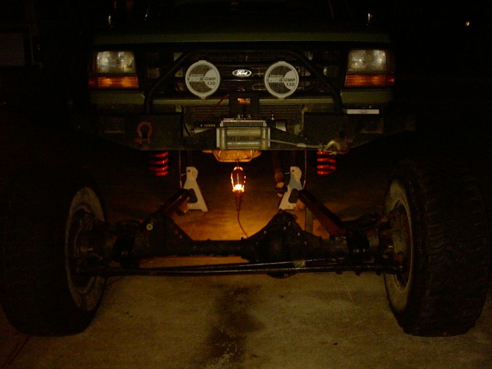 Ford truck on jack stands at night with solid front axle on the ground below its winch bumper
