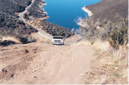 1988 Ford Bronco - A white pickup truck navigates a dirt road with a scenic lake view in the background.