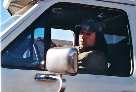 1988 Ford Bronco - A man with long hair and a camouflage hat drives a white truck.
