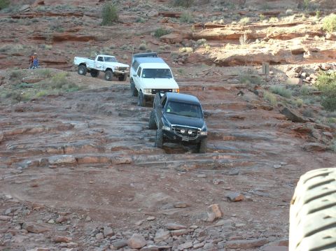 1993 Ford Bronco - Three off-road vehicles navigate a challenging rocky terrain in a desert landscape.