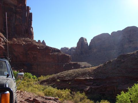 1993 Ford Bronco - An off-road vehicle is parked on a trail overlooking a vast desert canyon with red rock formations.