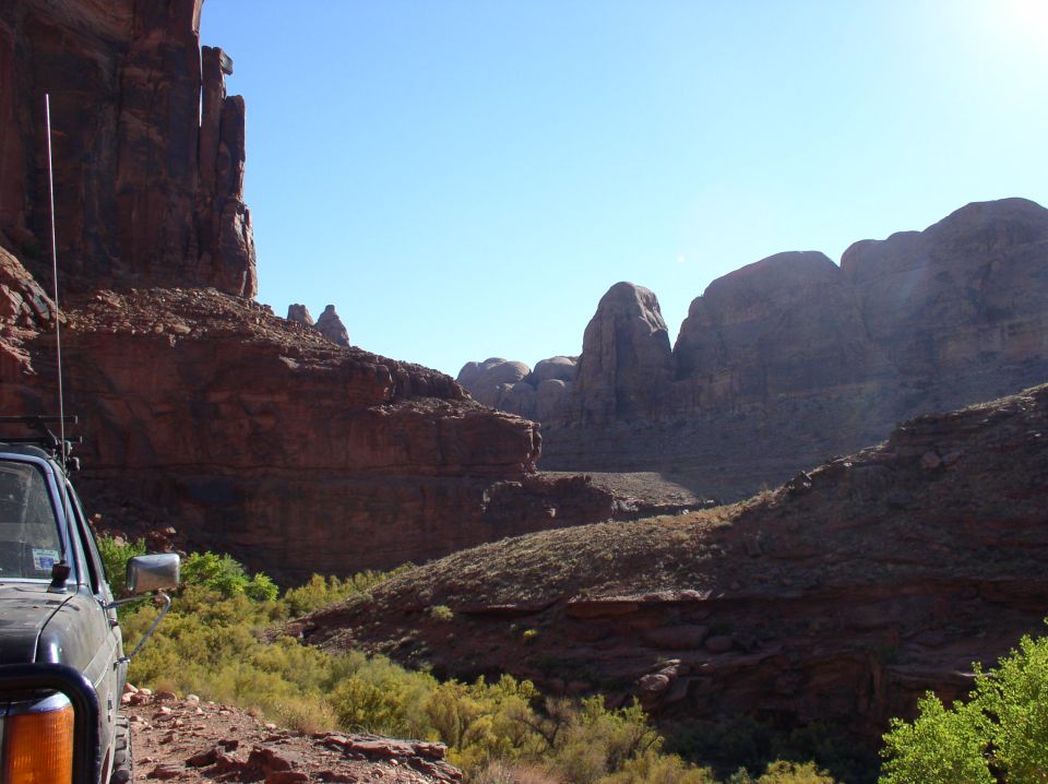Front corner of an off-road vehicle parked on a dirt track with red rock canyon scenery
