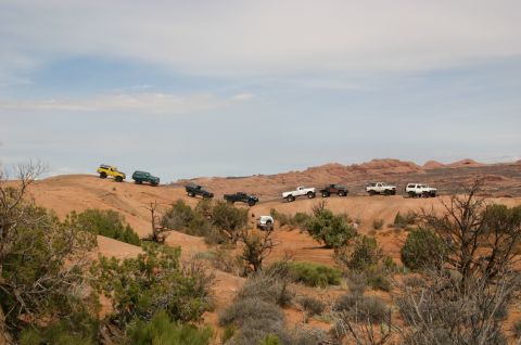 1993 Ford Bronco - A convoy of off-road vehicles navigates a desert trail under a partly cloudy sky.