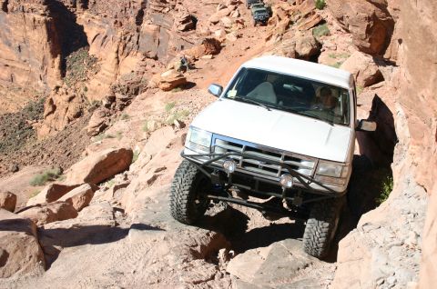1993 Ford Bronco - White 1993 Ford Bronco tackling a challenging Moab trail with other off-roaders following.