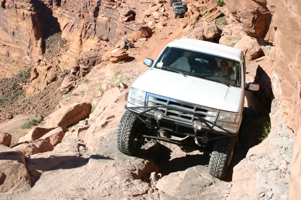 White lifted Ford Bronco descending red sandstone ledge on canyon trail