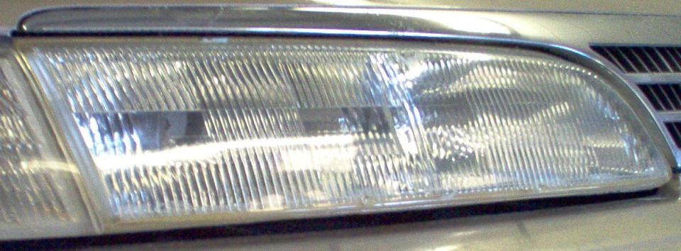 Clear composite headlight assembly on a silver car next to a vertical-slot grille