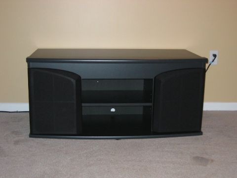 1985 Ford LTD Crown Victoria - A black entertainment center with integrated speaker enclosures and open shelving is shown against a tan wall.