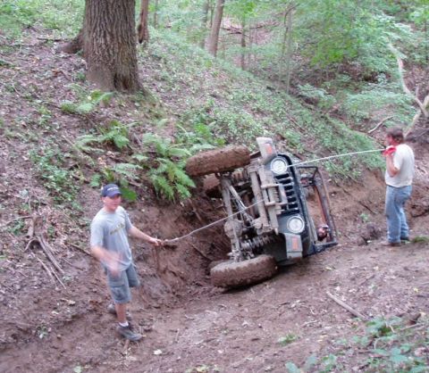 1992 Ford Bronco - Two people try to recover an off-road vehicle that has tipped onto its side on a steep, muddy incline.