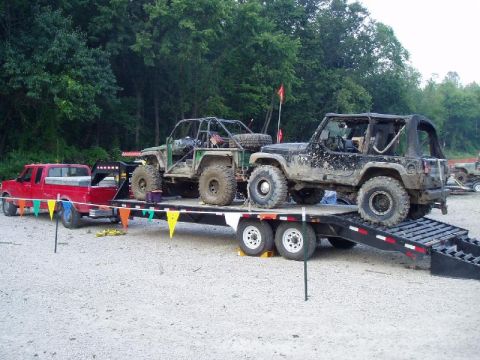 1992 Ford Bronco - Two heavily modified off-road vehicles are loaded onto a trailer towed by a red pickup truck.