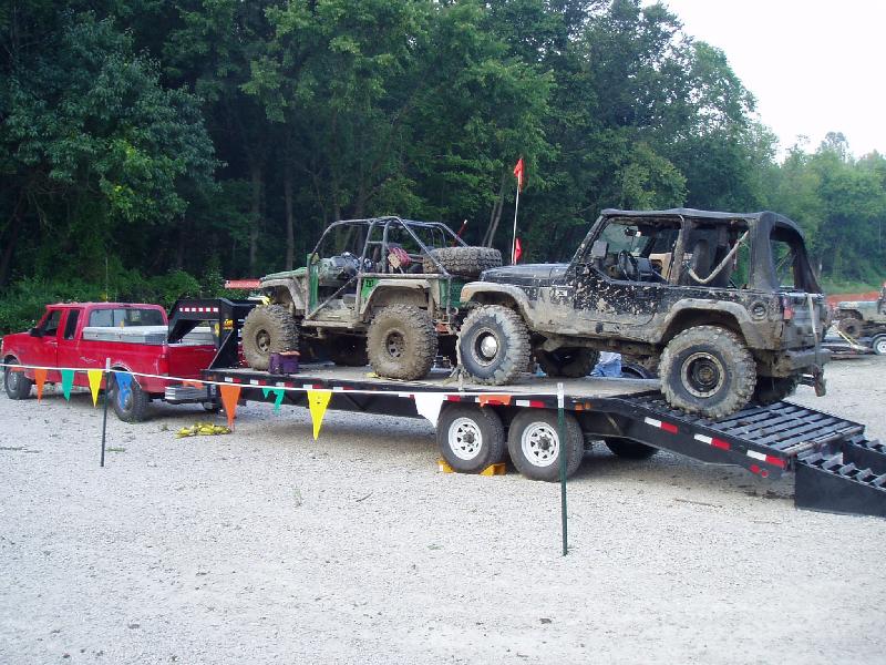 Red pickup truck towing a trailer with two muddy off-road vehicles