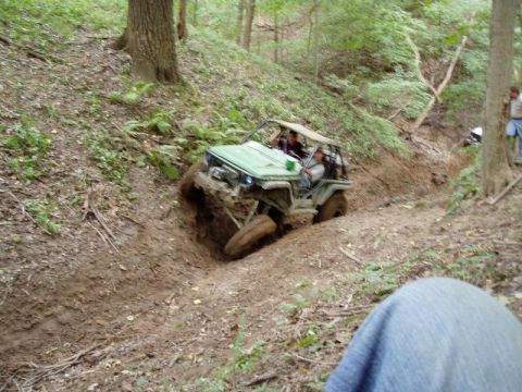 1992 Ford Bronco - An off-road vehicle navigates a challenging muddy terrain in a wooded area.