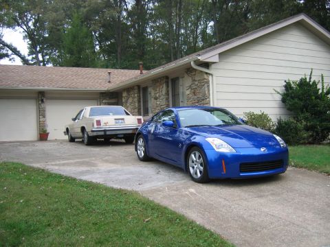 1985 Ford LTD Crown Victoria - Two cars are parked in a driveway in front of a house with a garage.