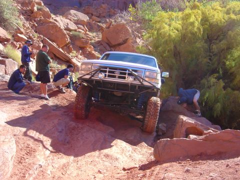 1993 Ford Bronco - A white Ford Bronco is driven over a challenging rocky obstacle with several people watching.
