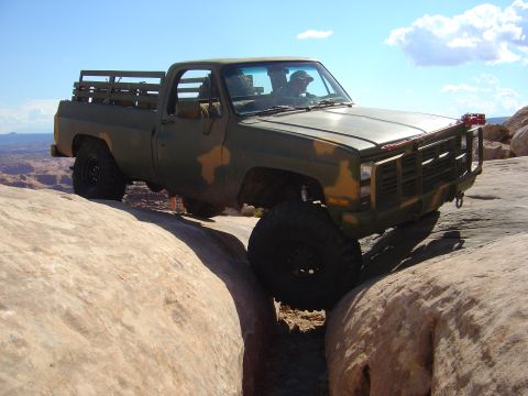 1993 Ford Bronco - This pickup truck is driving through a tight spot on a rocky trail under a clear blue sky.