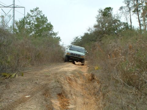 1994 Ford Bronco - Pickup truck navigates a challenging dirt path surrounded by dense vegetation and utility poles.