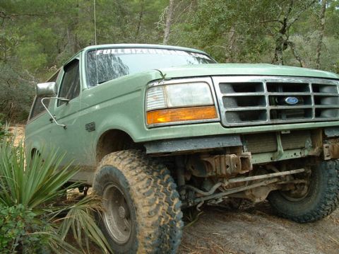 1994 Ford Bronco - This light green Ford Bronco is shown off-road with large, mud-covered tires and a banner across the windshield.