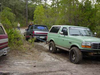 1994 Ford Bronco - Two SUVs are on a dirt road, one towing the other through a wooded area.