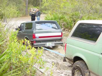1994 Ford Bronco - Two Ford Broncos are stuck in the mud on a wooded trail, with one vehicle towing the other.