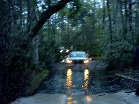 1994 Ford Bronco - Multiple vehicles navigate a waterlogged path in a wooded area.