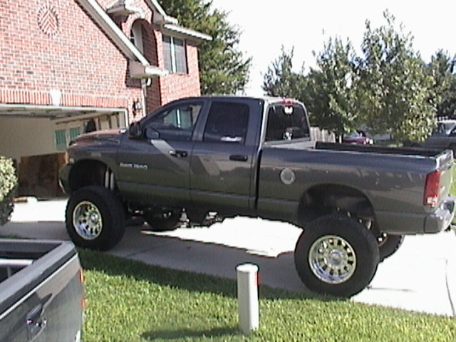 Gray lifted Dodge Ram quad-cab pickup parked in a driveway in front of a two-story brick house
