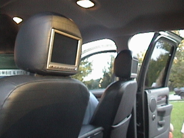 Truck interior with a flip-up LCD screen mounted in a headrest, door open to trees outside