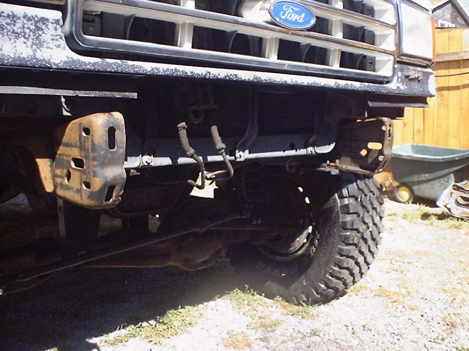 Front end of a Ford truck, missing bumper, showing suspension and tire
