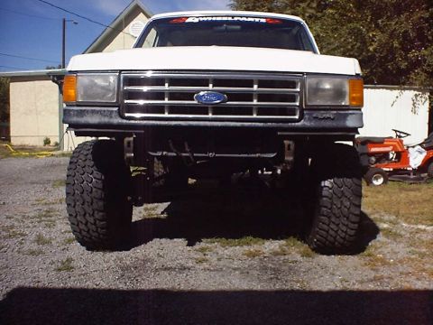 1988 Ford Bronco - Front view of a lifted white Ford truck with a chrome grille and "4 WHEELPARTS" banner on the windshield.