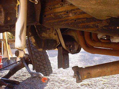 1988 Ford Bronco - Undercarriage view of a vehicle undergoing front suspension work, revealing rusty components and a removed driveshaft.