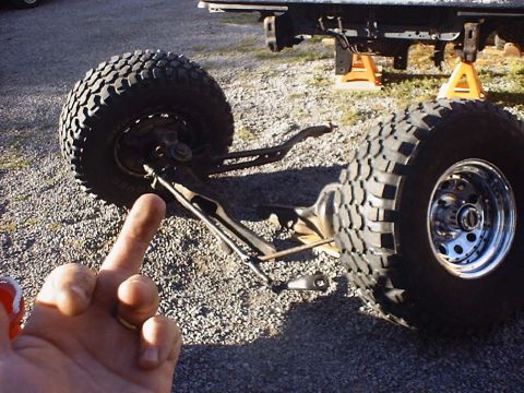 1988 Ford Bronco - Front suspension components and large off-road tires are shown, with a portion of the vehicle frame elevated on jack stands.