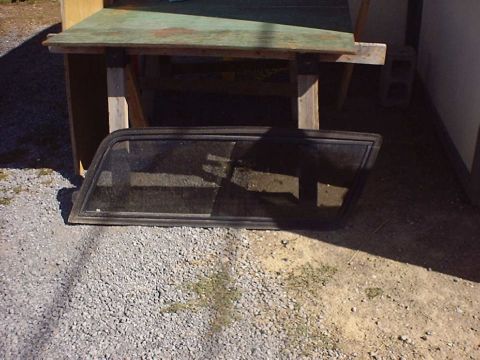 1988 Ford Bronco - Car window part resting on gravel outdoors.