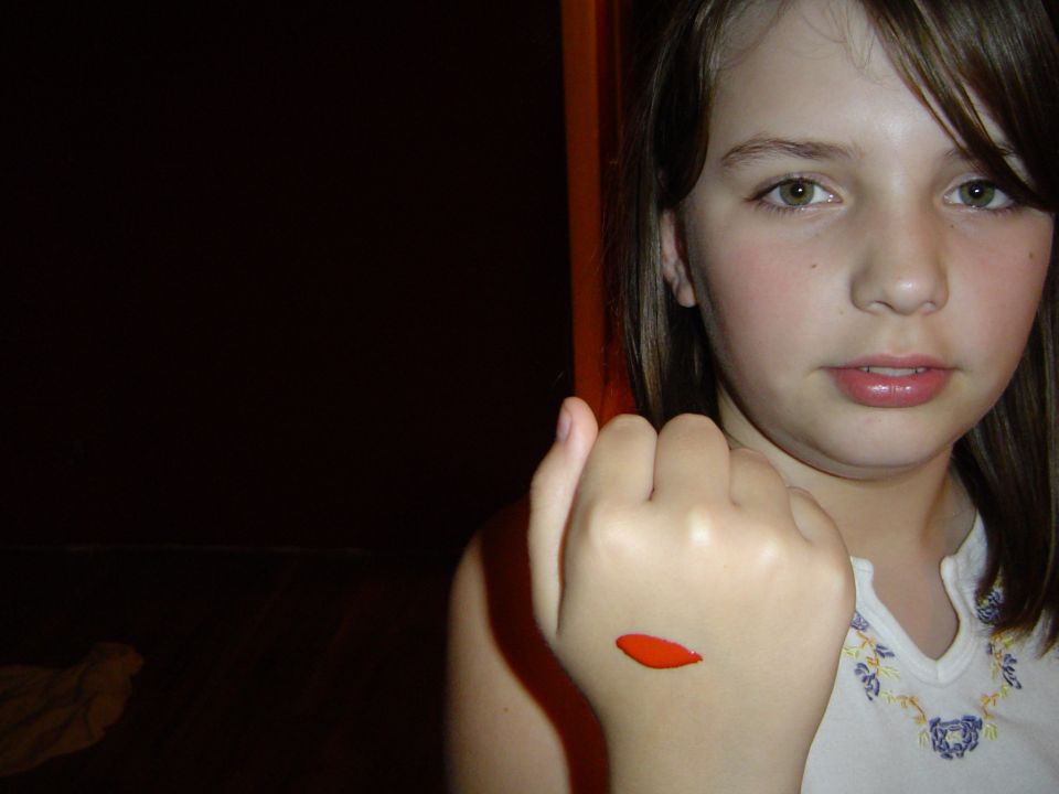 Young girl indoors holding out her hand showing a small orange seed or petal on the skin