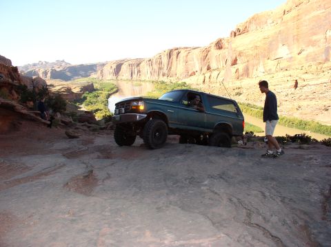 1993 Ford Bronco - A green SUV navigates a rocky path with a river and canyon in the background.