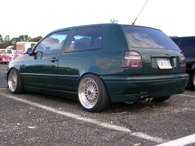 Green Volkswagen Golf Mk3 hatchback with aftermarket wheels and dual exhaust pipes, viewed from the rear